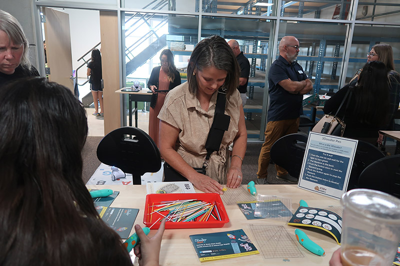 An attendee looking at the items they 3D printed with a pen on an activities table.
